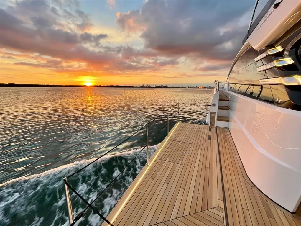 Luxury yacht deck during sunset, reflecting golden hues on the water with distant skyline views and gentle waves.